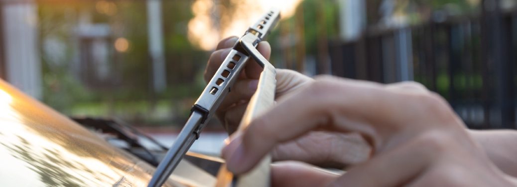 Hands pick a windshield wiper up off the windshield, presumably for the purpose of replacing it.