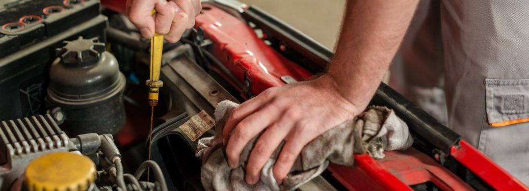 A man's hands check oil under the hood.
