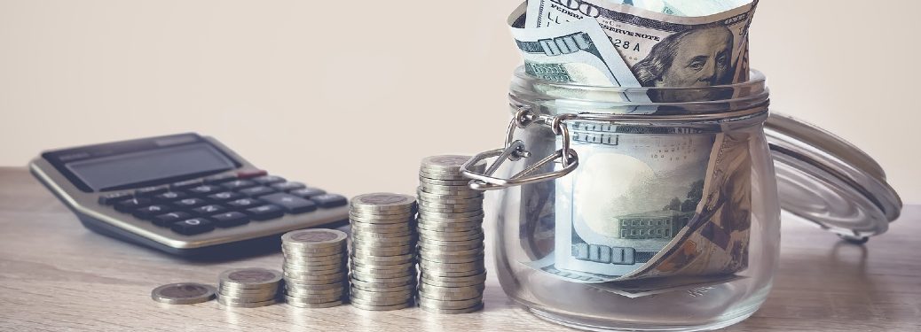 Calculator sitting by coin stacks and jar of money