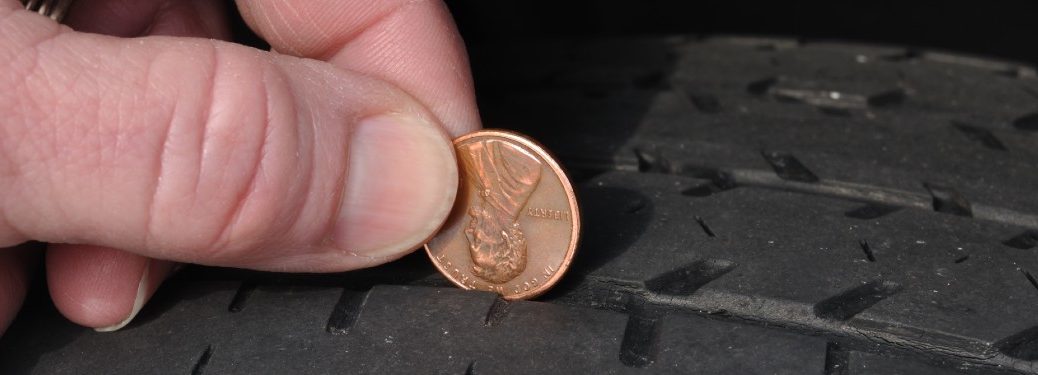 someone using a penny to check the tread of a tire