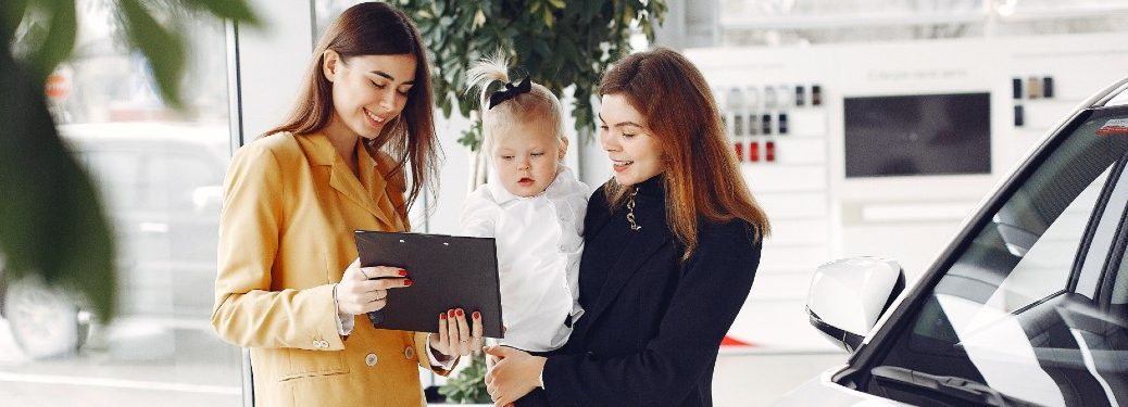 woman dealer showing vehicle info to mother with baby at dealership