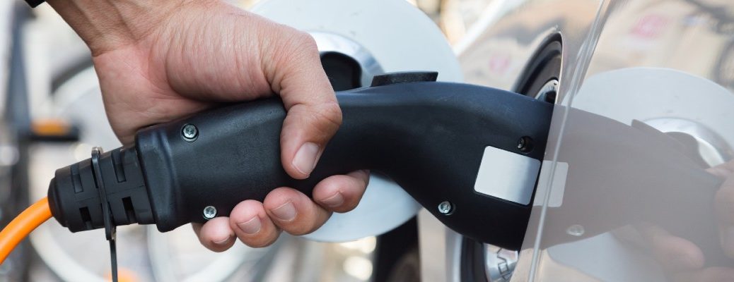 A stock photo of a person plugging in an electric vehicle to charge its battery.