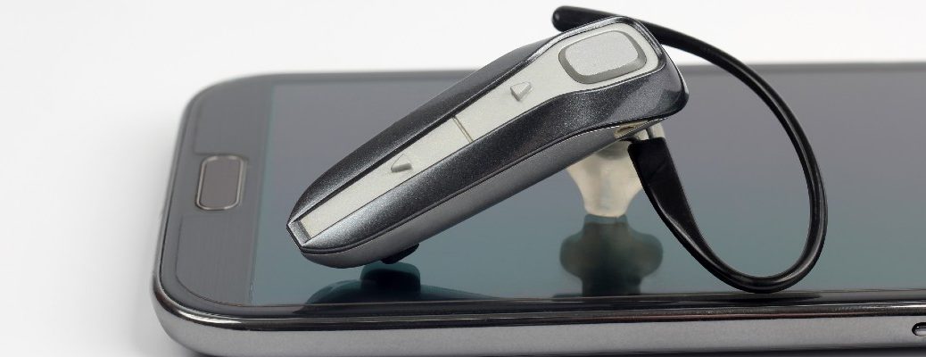 A stock photo of a smartphone and a Bluetooth ear piece.