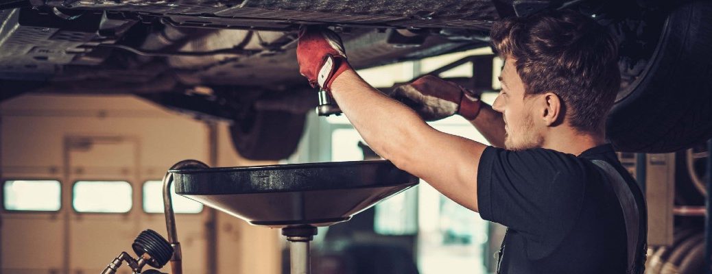 A stock photo of a person draining the oil from a vehicle.