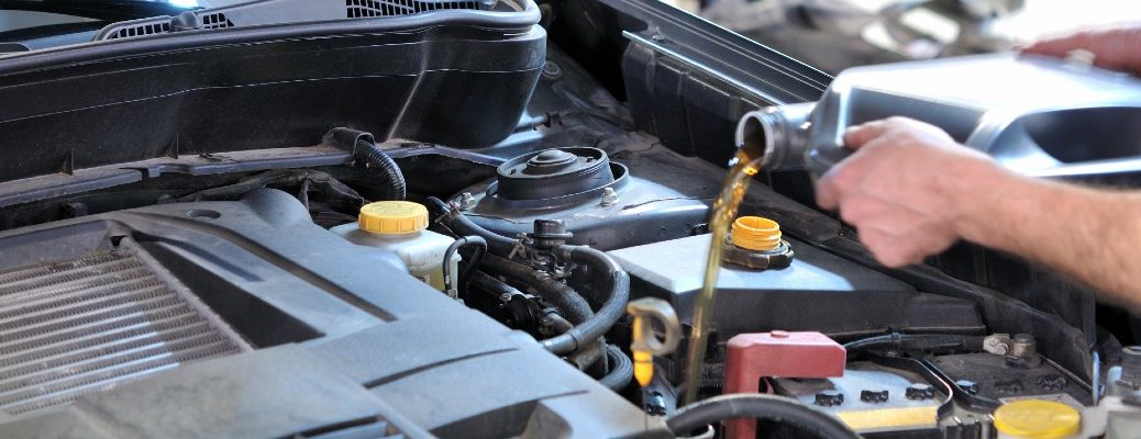 A stock photo of a person pouring motor oil into an engine.