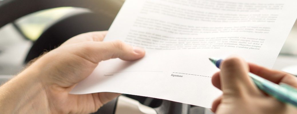 A stock photo of a person signing a contract in their car.