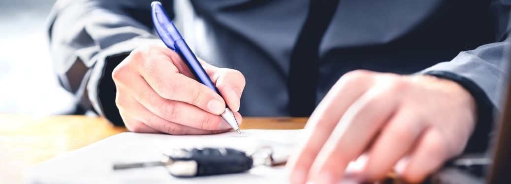 Man signing an auto loan agreement with a key in the foreground