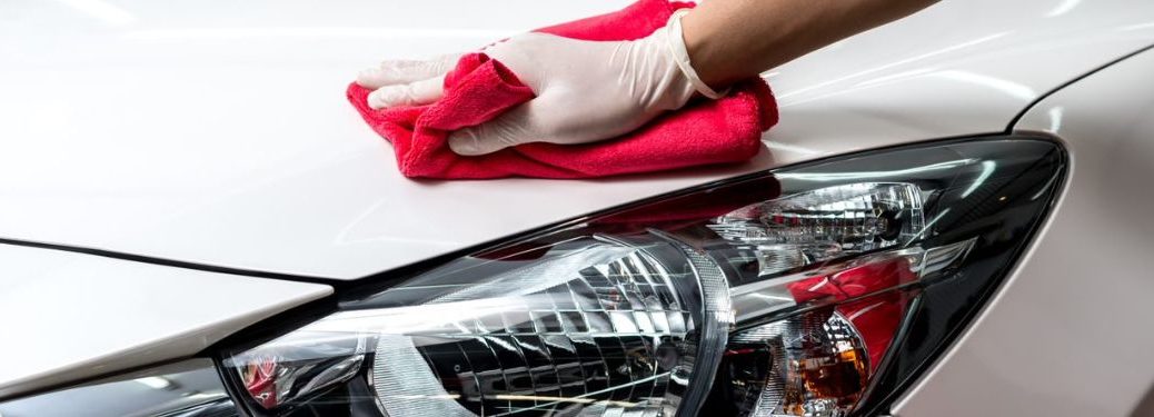 Close up of a hand cleaning a white car using a red cloth