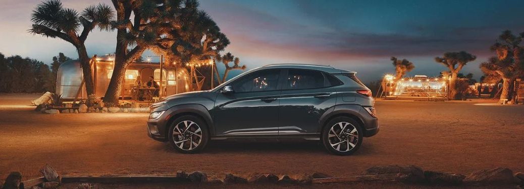 One dark green color 2022 Hyundai Kona is parked in a desert land while a couple is having a dinner date in the background.