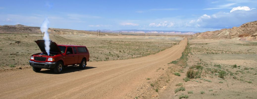 A photo of an overheating pickup truck on the side of a dirt road