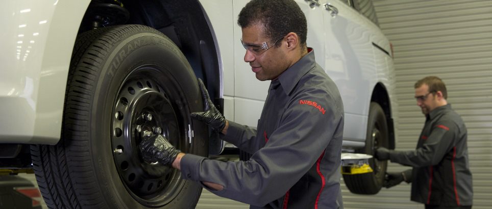 A car mechanic is working on the tire of a white car