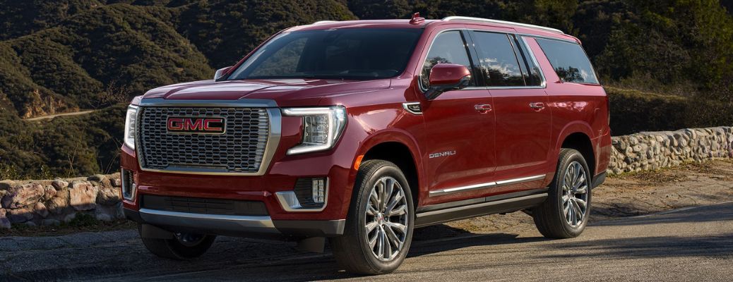 Red Yukon Parked On-Road Next to Stone Wall with Hills
