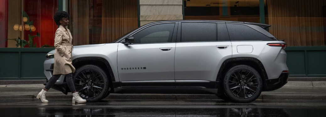 A woman walking past a 2024 Jeep Wagoneer S parked on a rainy street.