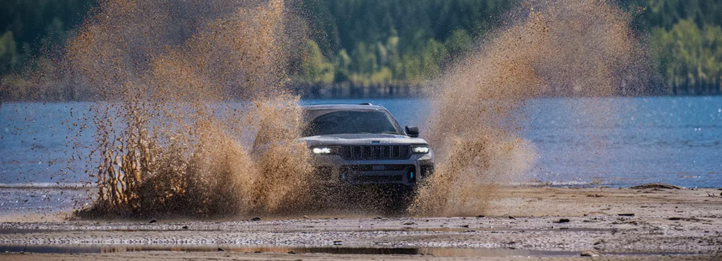 2025 Jeep Grand Cherokee is captured mid-action, driving through a muddy terrain near a lake