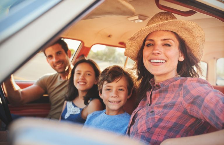 Family of four sitting inside a car and smiling