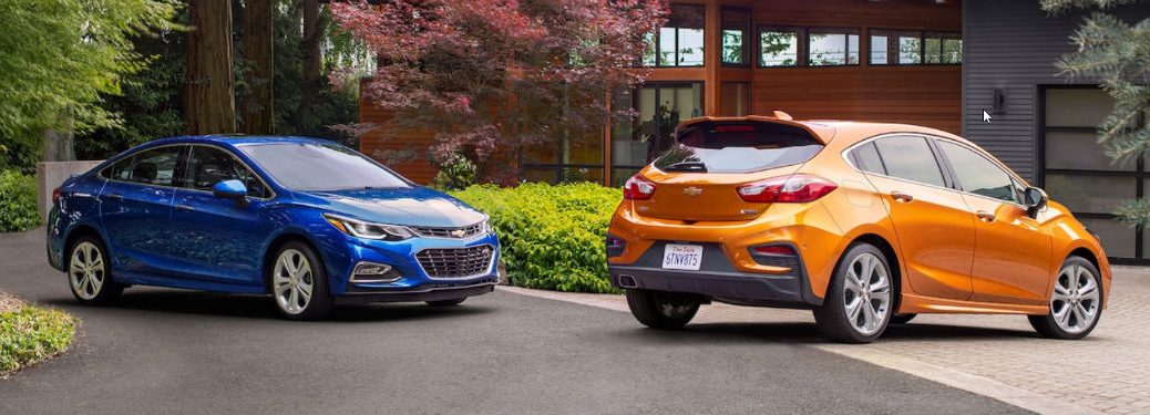 Passenger side exterior view of a blue 2018 Chevy Cruze sedan next to a rear exterior view of a orange 2018 Chevy Cruze hatchback