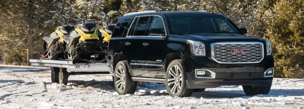 Passenger side view of a black 2018 GMC Yukon hauling snowmobiles