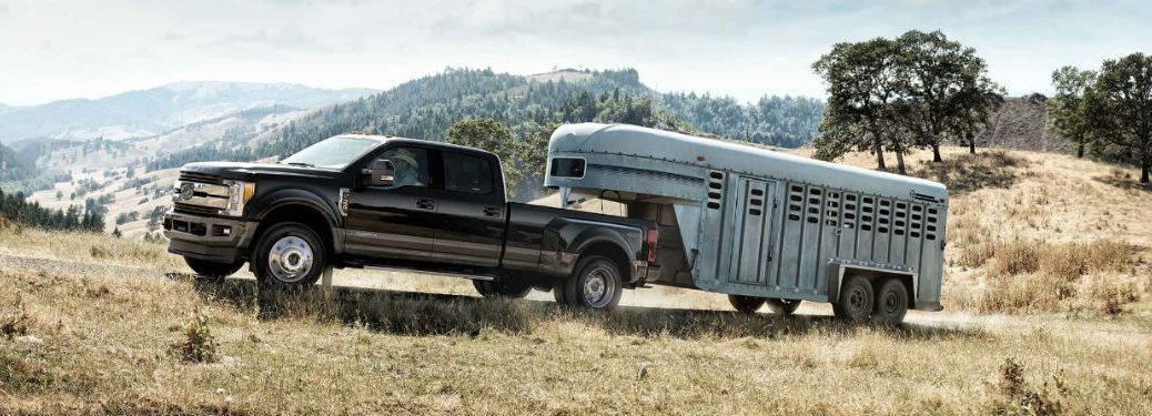 Driver side exterior view of a black 2018 Ford F-350 towing a large trailer