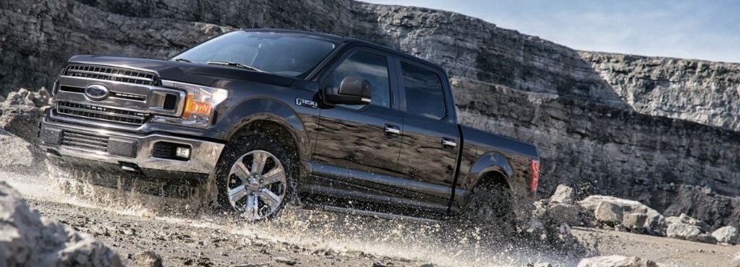 2020 Ford F-150 driving through mud with a cliff in background from front driver side angle_o