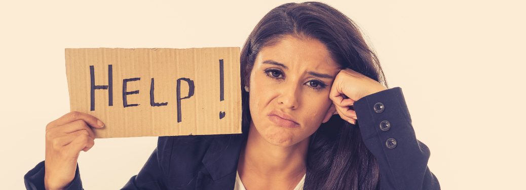 A puzzled woman holds a cardboard sign with the word "help" written on it in marker.