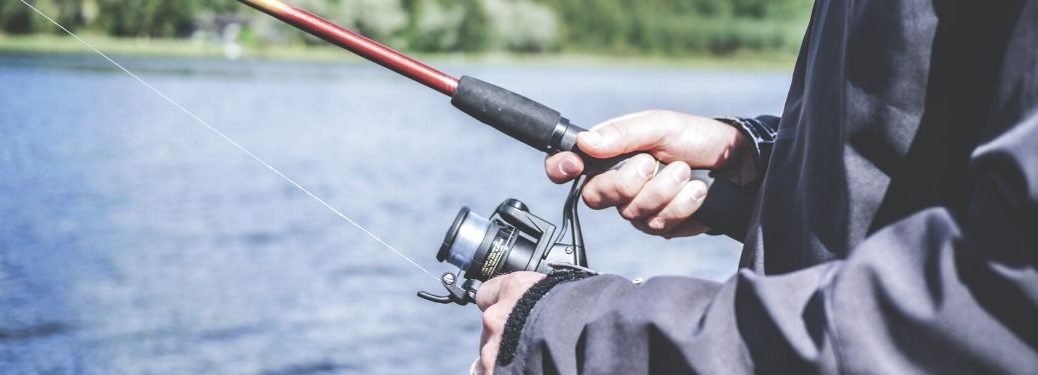 Close-up on a mans hands warmly holding a fishing pole at a lake.