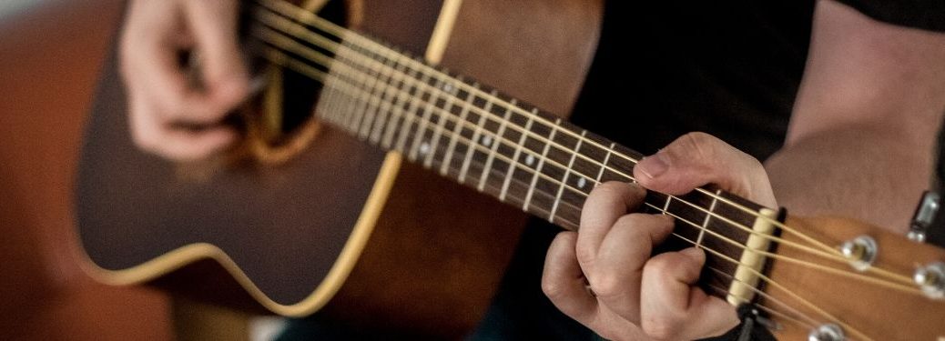 Two hands play an acoustic guitar