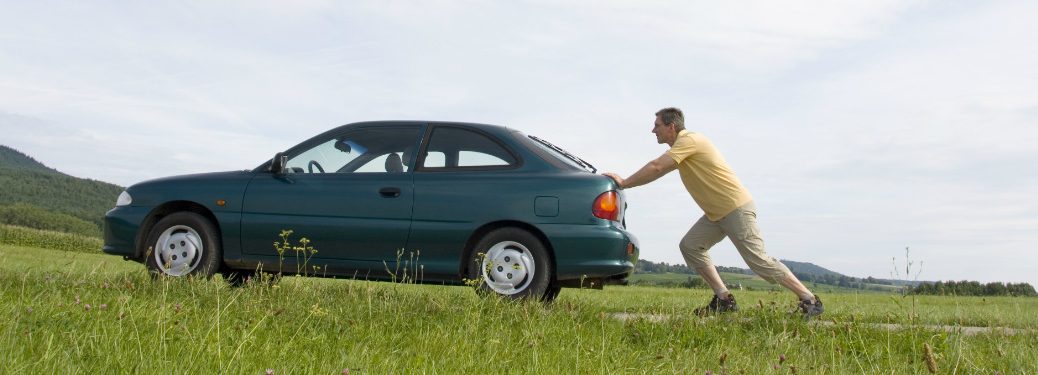 Man pushes a car along a road.