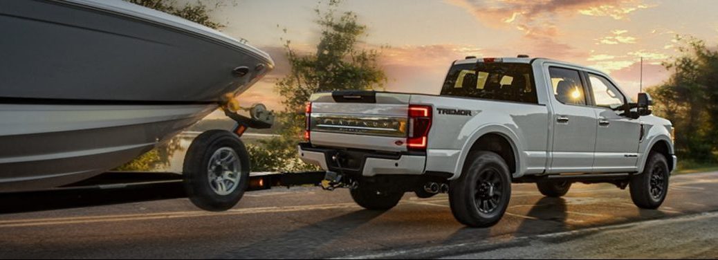 White 2020 Ford F-350 Super Duty pickup tows a boat along a highway at sunset