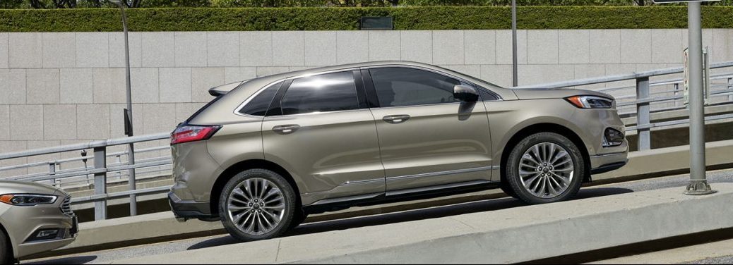 Tannish-colored 2020 Ford Edge drives up a highway at an inclined angle.