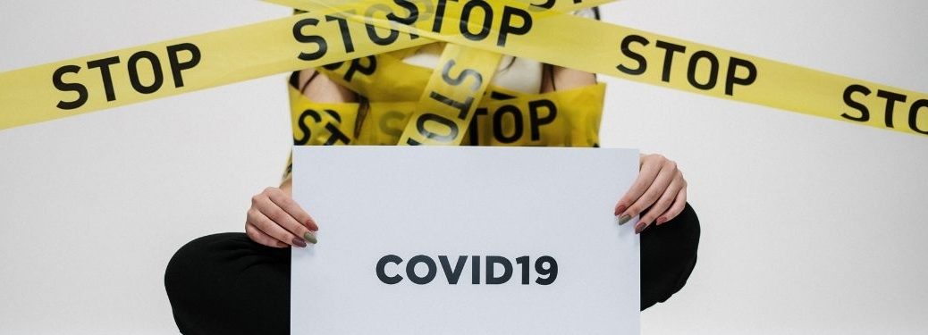 Caution tape reads, "Stop"; a sign below reads, "COVID19"