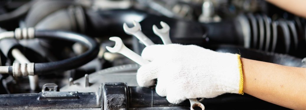Mechanic holding wrenches by a car engine