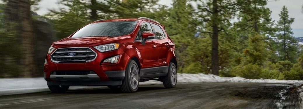 A red 2021 Ford EcoSport driving on a road surrounded by trees