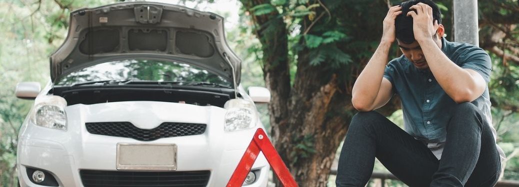 A person sitting in front of a broken car.
