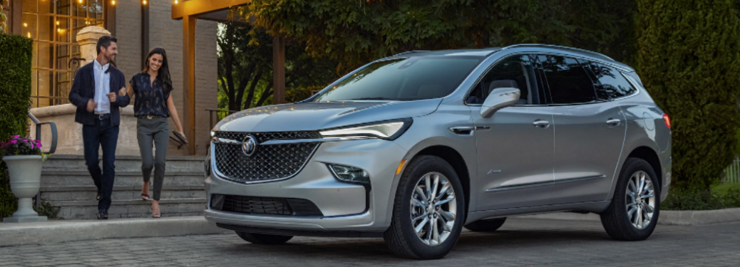A couple moving towards the 2022 Buick Enclave which is parked in front of a building