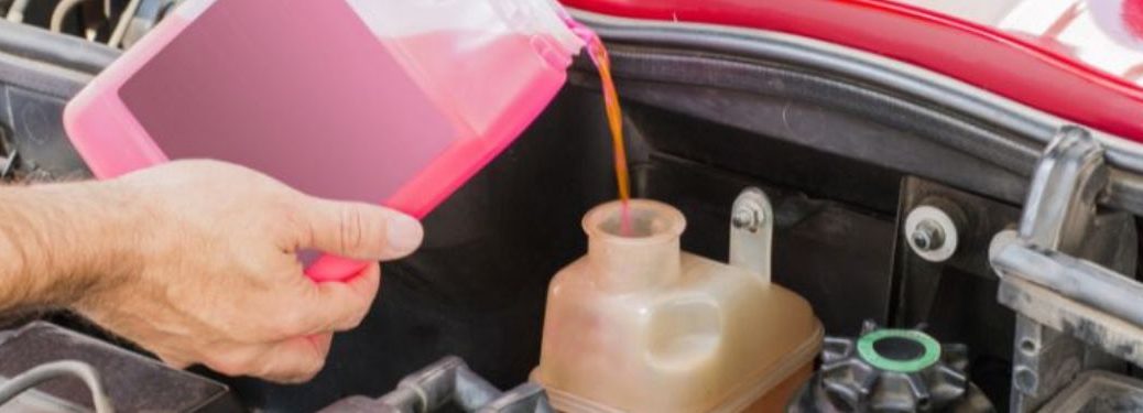 Mechanic topping up engine coolant in the vehicle