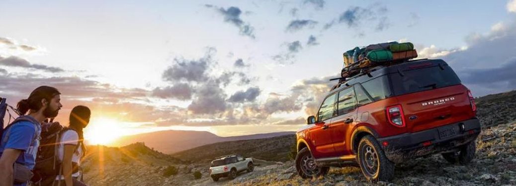 A red 2023 Ford Bronco Sport carrying luggage and a few people walking past it.