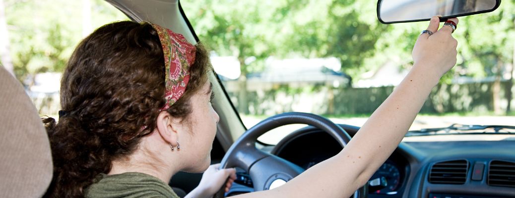 a young girl in driver seat adjusting the rearview mirror of a car
