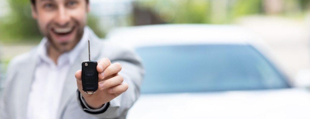 A man holding a set of car keys by a white car
