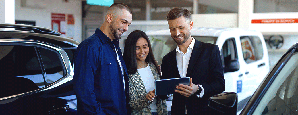 three people at an automotive dealership looking at a tablet