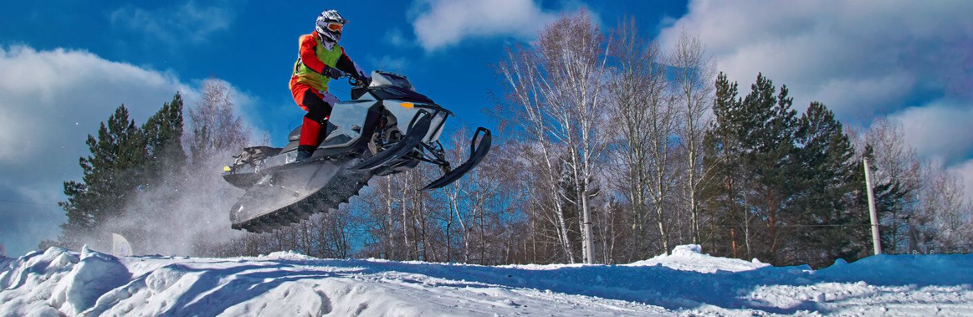 Man jumping snowmobile over hill