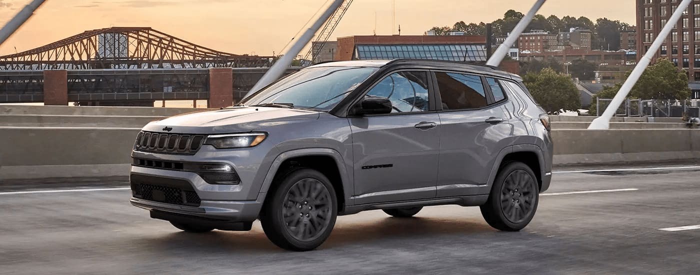 A grey 2023 Jeep Compass SUV for sale near Elizabeth on a bridge during a test drive.