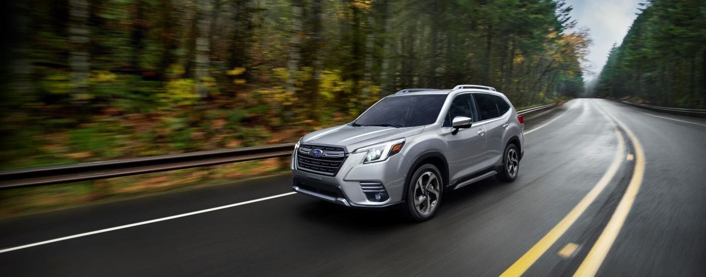 A silver 2023 Subaru Forester driving on a winding road lined with trees after viewing cars for sale.