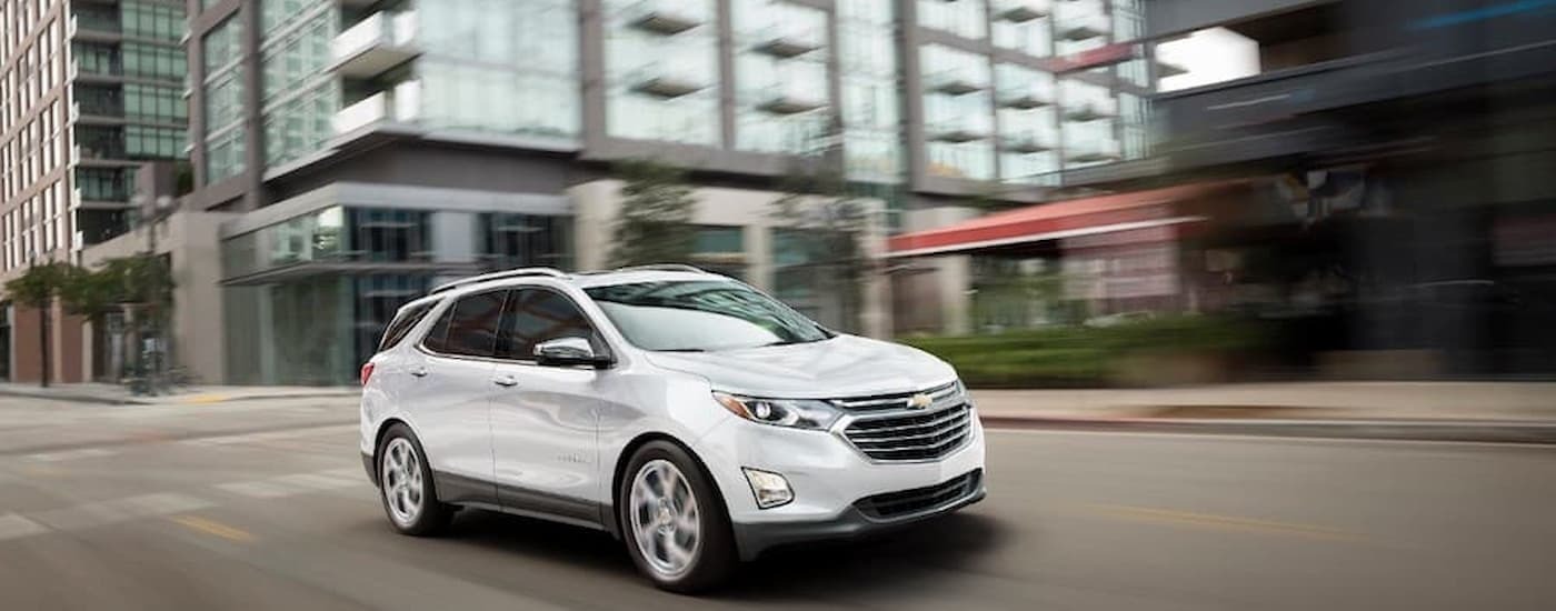 A white 2018 Chevy Equinox driving on a city street after viewing cars for sale in Jersey City.