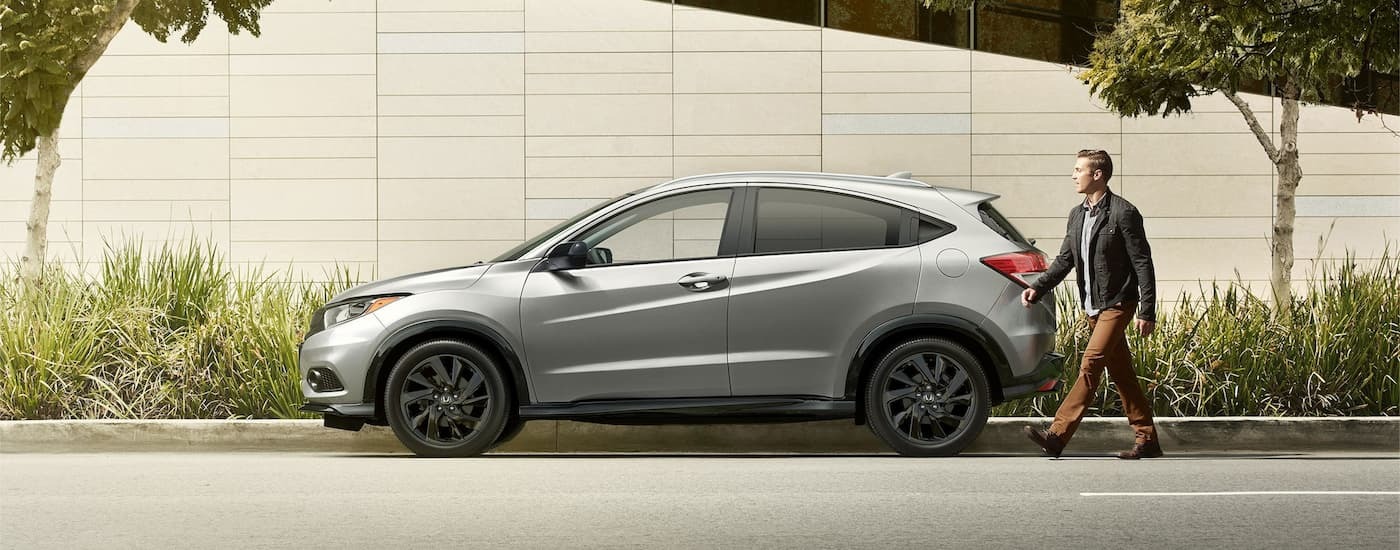 A silver 2022 Honda HR-V is parked on the side of a city street as a man walks by.