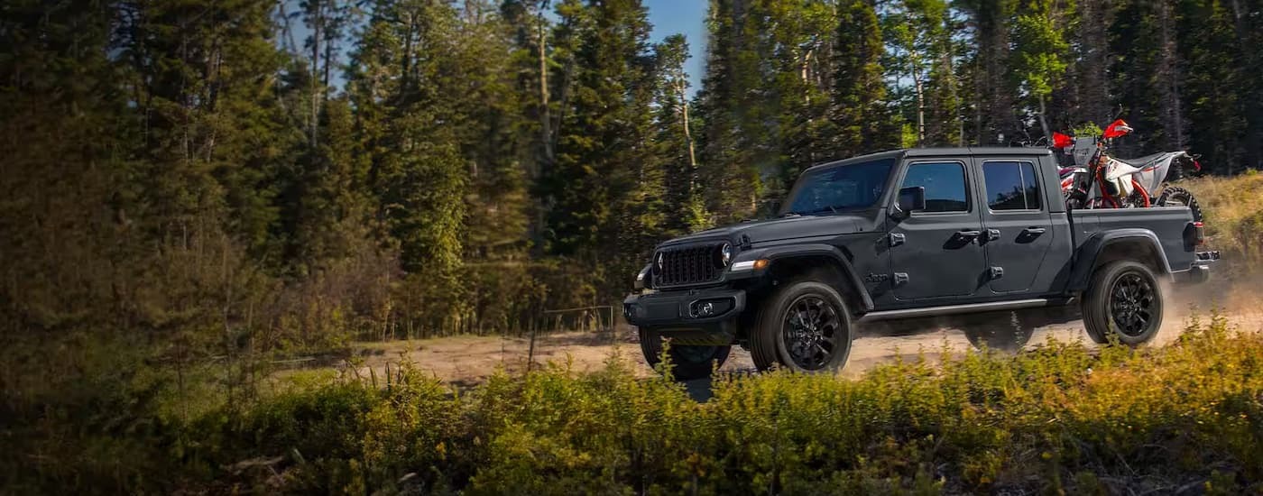 Grey 2023 Jeep Gladiator with dirt bikes in the bed driving on a dirt road
