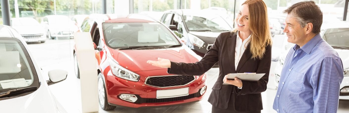 Man Standing With Saleswoman Who Is Pointing At A Car