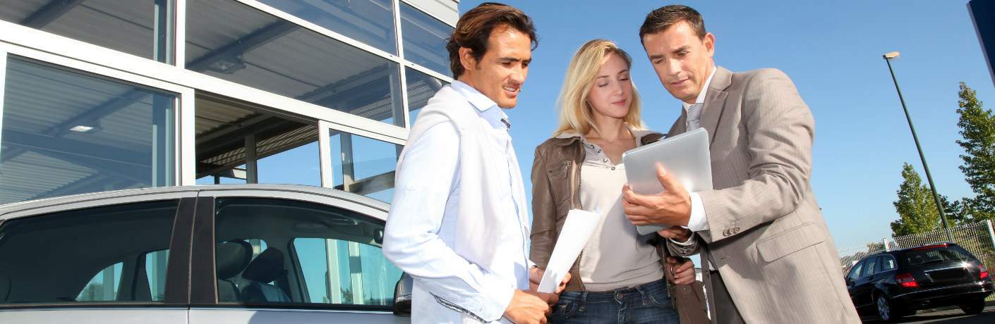 salesperson talking to a couple at car dealership outside