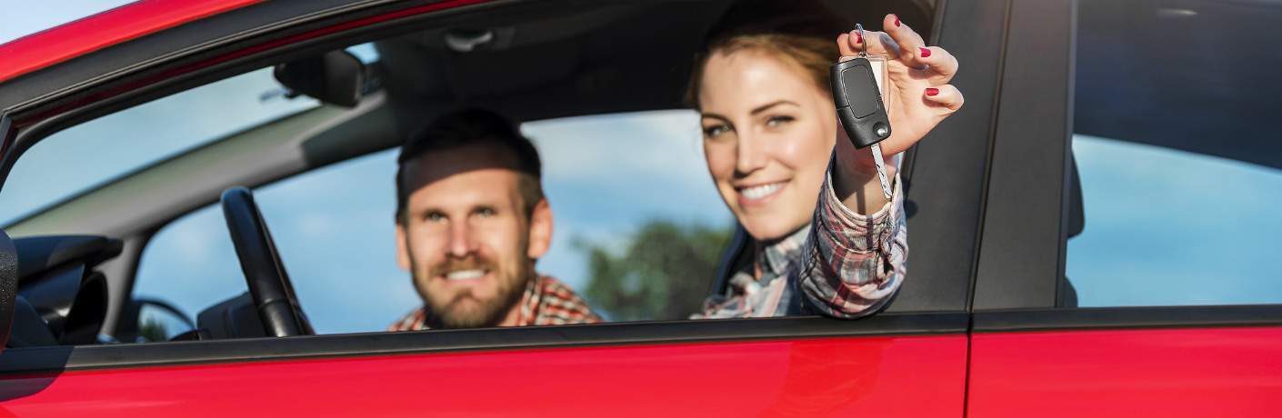 young couple in vehicle smiling and showing keys
