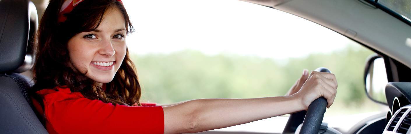 young woman behind wheel of car smiling at camera