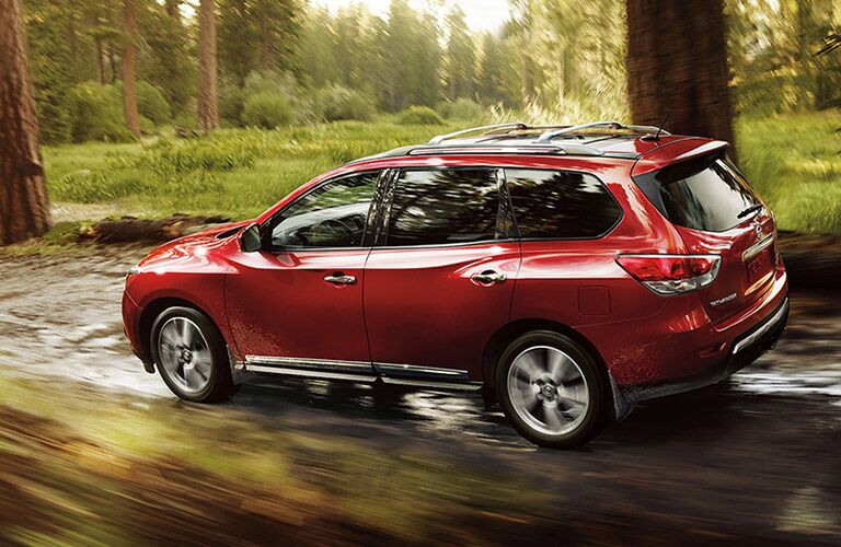 side view of a red 2016 Nissan Pathfinder driving through the forest